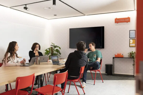 Vier mensen zitten in een vergaderruimte aan de Aert van Nesstraat bij Microlab, in gesprek rond een tafel met laptops.